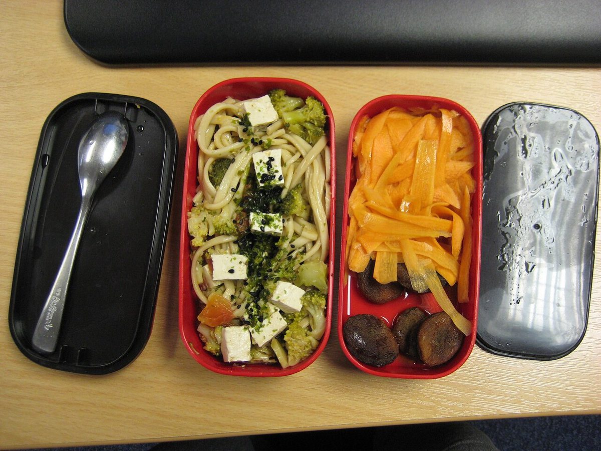 A compartmented lunch box holding noodles, vegetables, and carrots