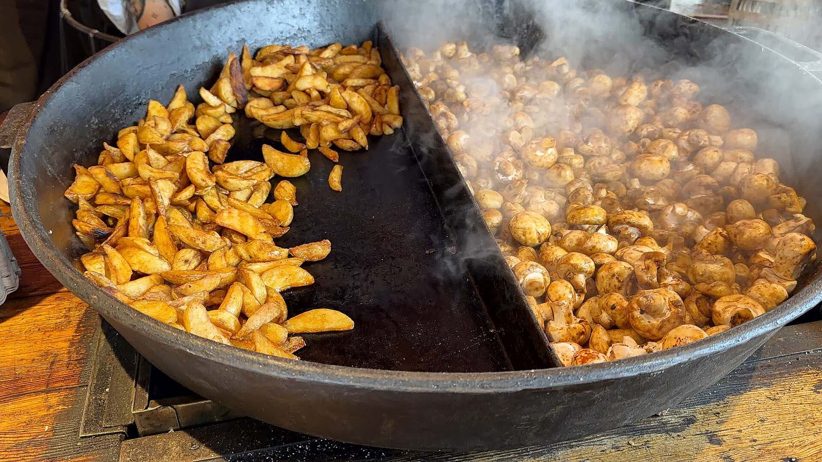 Fried potatoes and mushrooms cooking in a large black cast iron pan