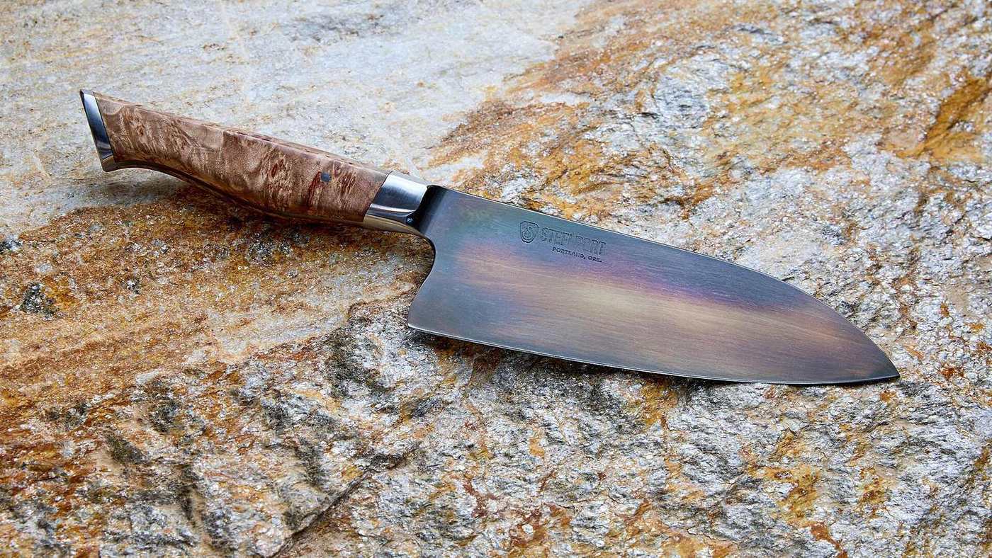 A chef's knife with a wooden handle resting on a stone surface