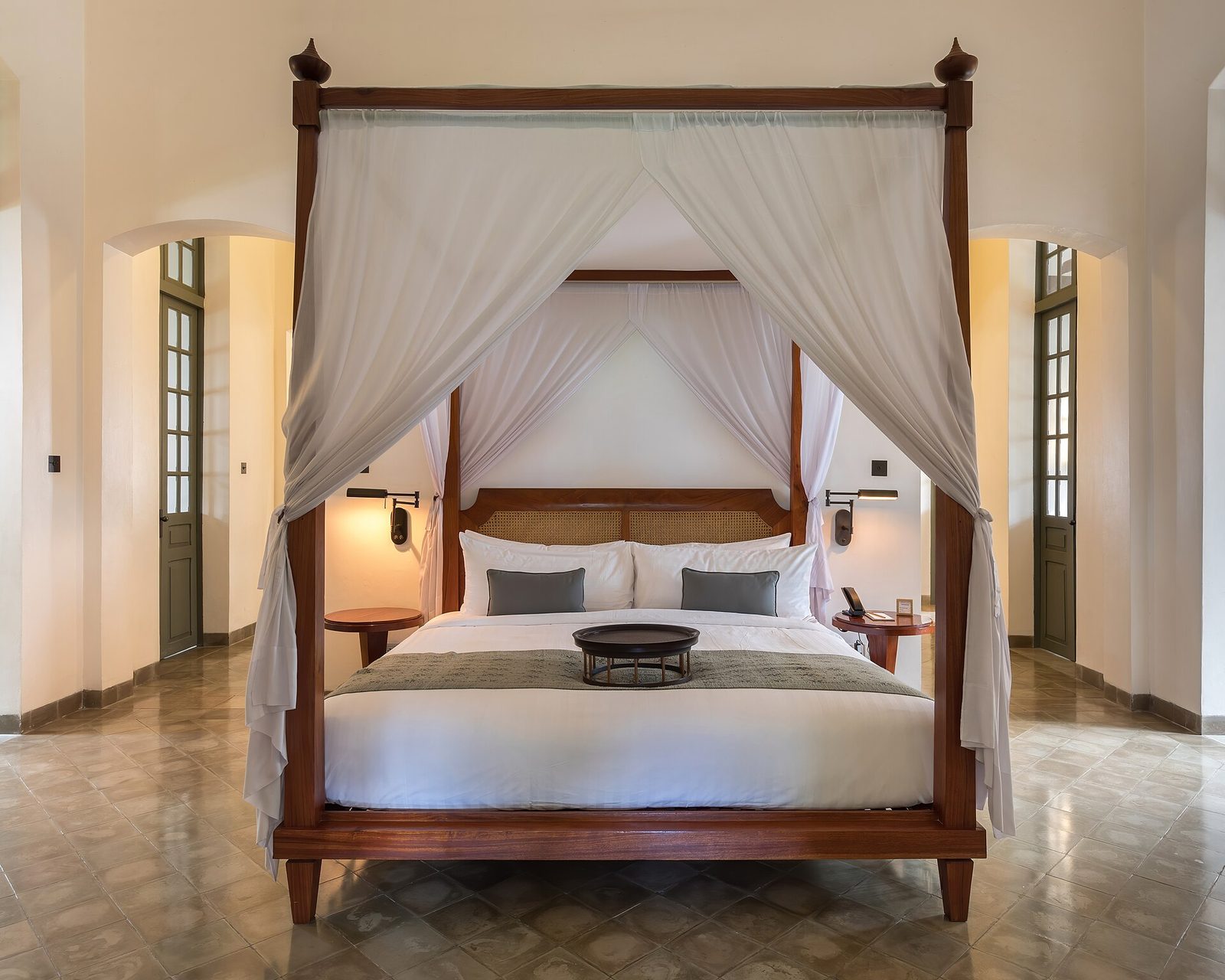 A wooden four-poster bed with white bedding in a bright, airy room