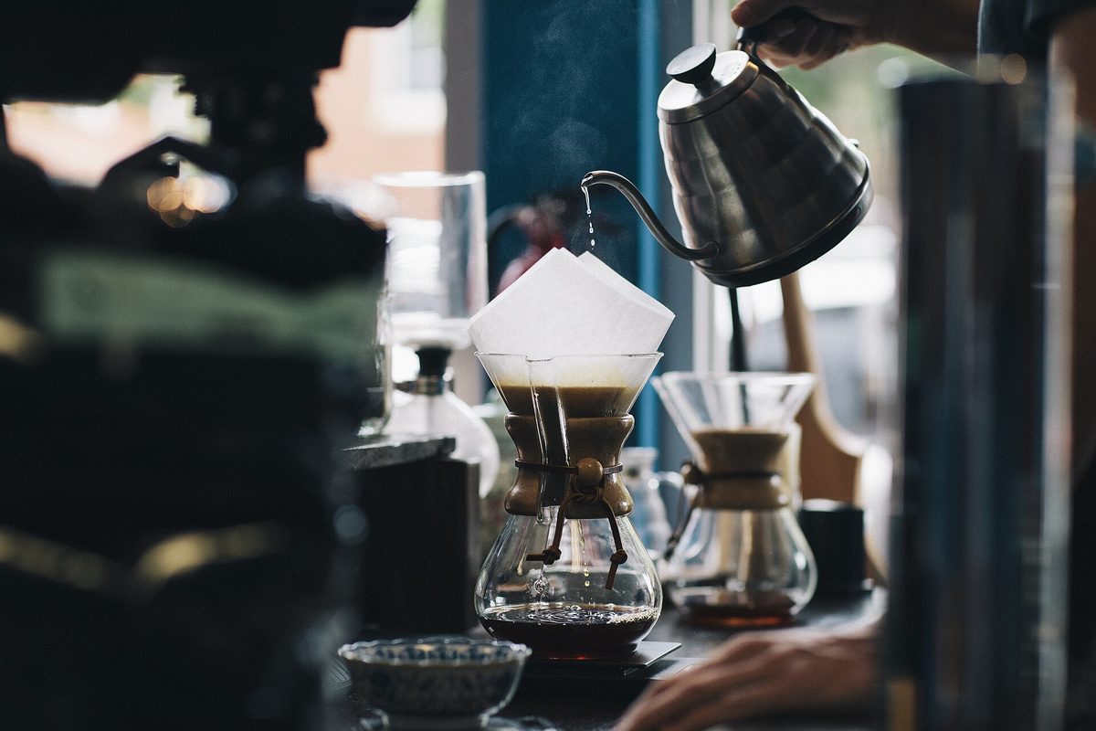 Water pouring from a gooseneck kettle into a cone filter over a glass carafe