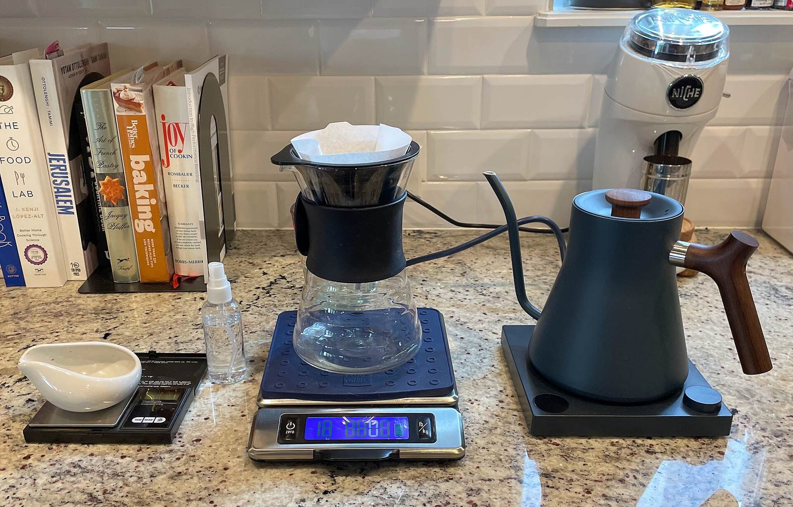 A pour-over coffee setup with a dripper, scale, gooseneck kettle, and grinder